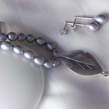 Load image into Gallery viewer, Grey pearls knot necklace, leaf silver pendant necklace placed on a white bottle of perfume, and a pair of oval grey pearls earrings,  on white satin fabric