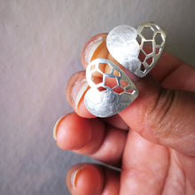 Load image into Gallery viewer, Hand holding a pair of silver heart stud earrings, on white background