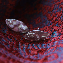 Load image into Gallery viewer, Two metallic leaf-shaped objects on a red and blue patterned fabric background