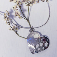 Load image into Gallery viewer, Sterling silver heart pendant with a red garnet cabochon, placed on a branch of dried white flowers, white background