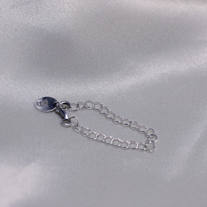 Silver chain extender placed on  white satin backdrop