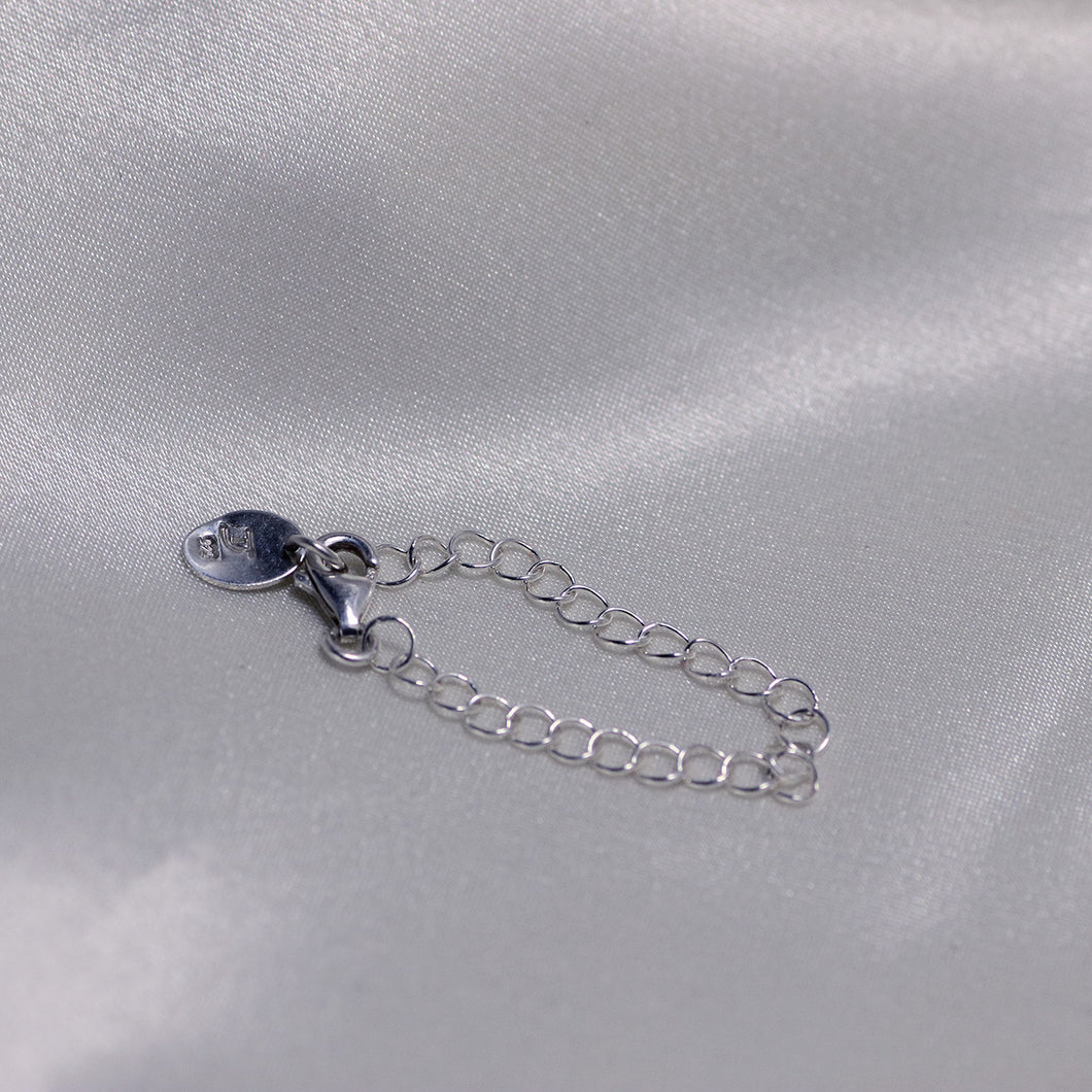 Silver chain extender placed on  white satin backdrop