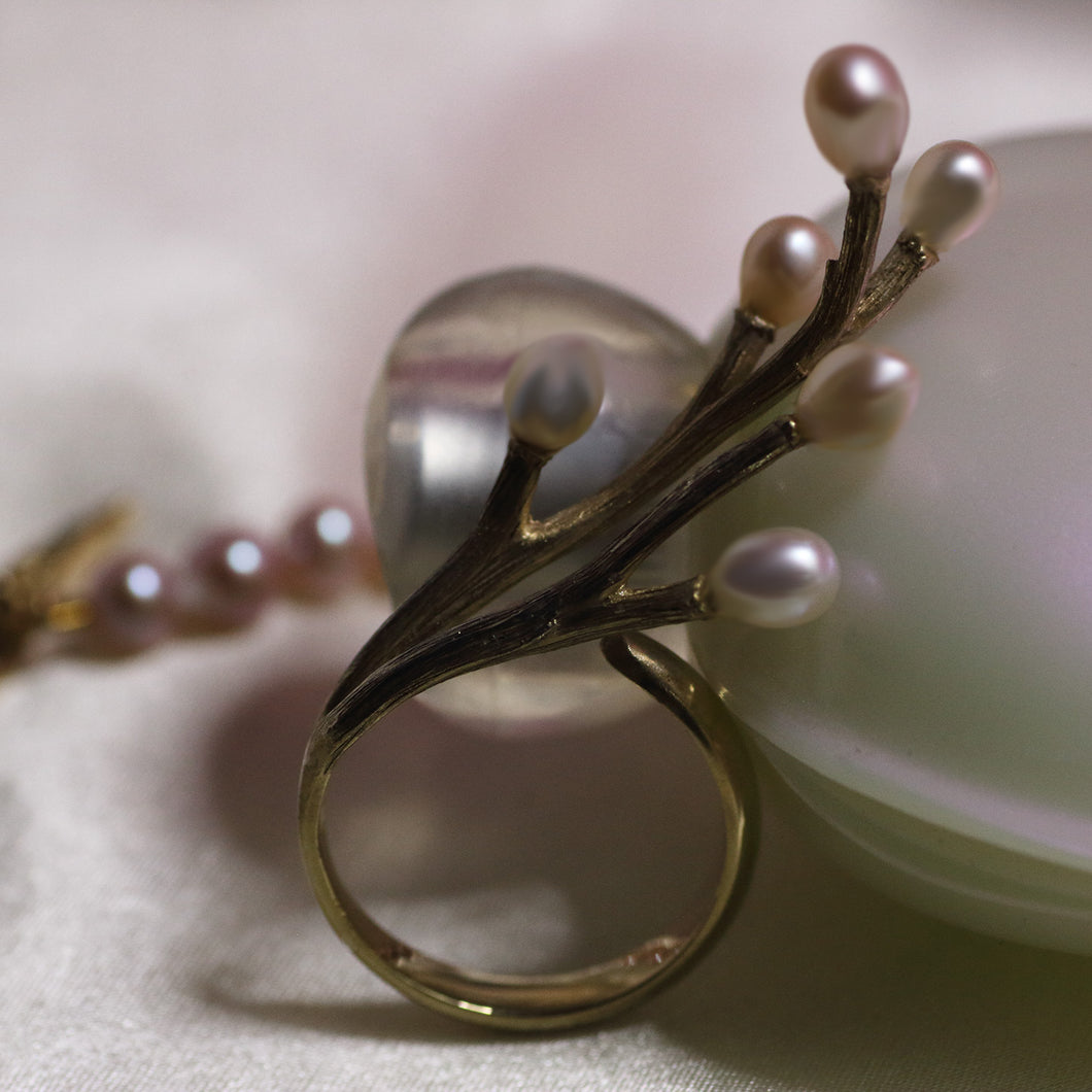 Closer shot on vermeil yellow gold ring with twig design standing against white bottle of perfume, pink pearls in the background