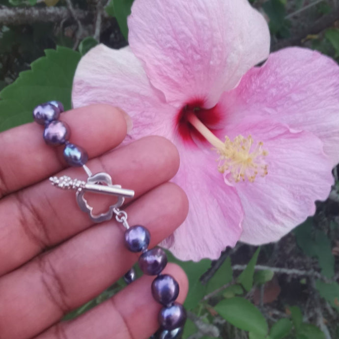 Knotted pearl bracelet placed on finger tips with pink hibiscus in background