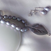 Load image into Gallery viewer, Grey pearls knot necklace, leaf silver pendant necklace placed on a white bottle of perfume, and a pair of oval grey pearls earrings,  on white satin fabric
