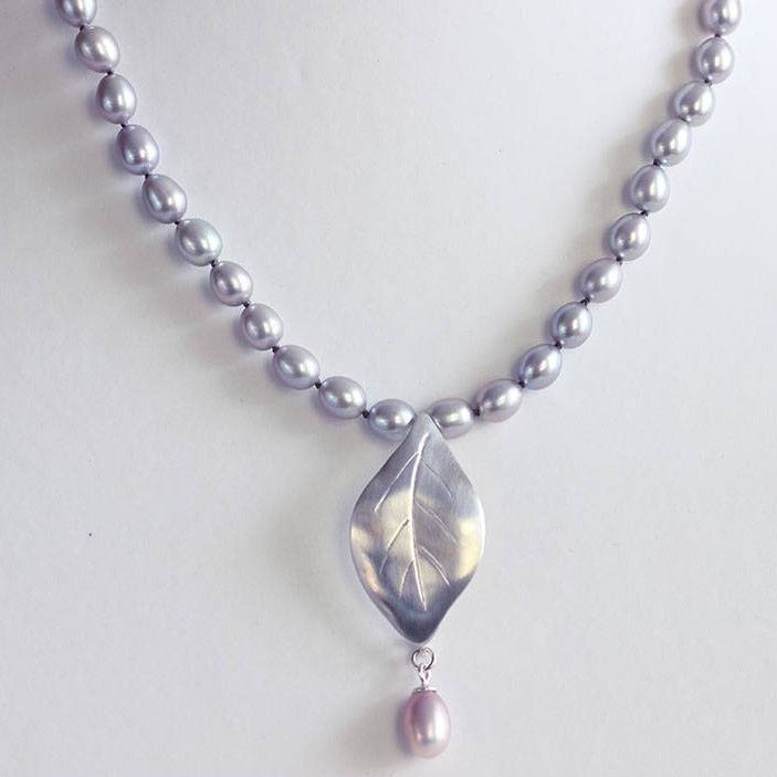 Grey pearls knot necklace, leaf silver pendant necklace placed on a jewelry  bust display