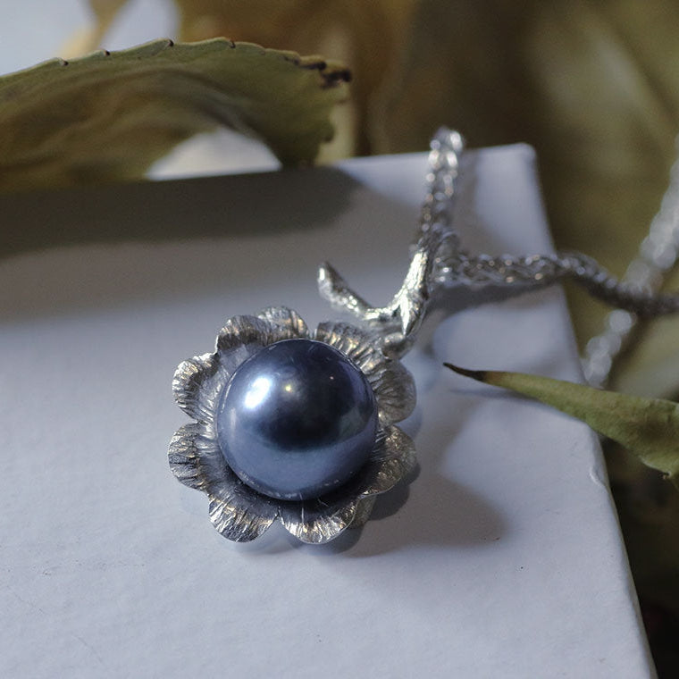 Silver flower pendant, black pearl, white background, dried leaves in the back