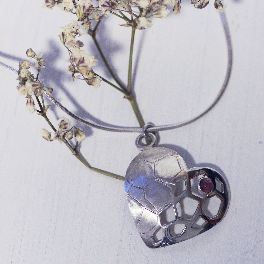 Sterling silver heart pendant with a red garnet cabochon, placed on a branch of dried white flowers, white background