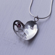Load image into Gallery viewer, Sterling silver heart pendant with a red garnet cabochon, face down on white background
